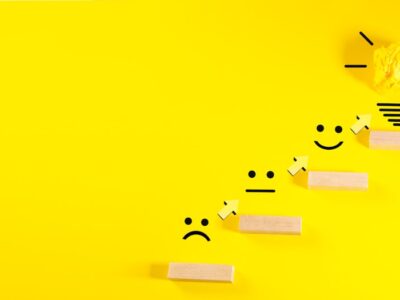 Wooden blocks with smiley faces ascending towards a lightbulb.